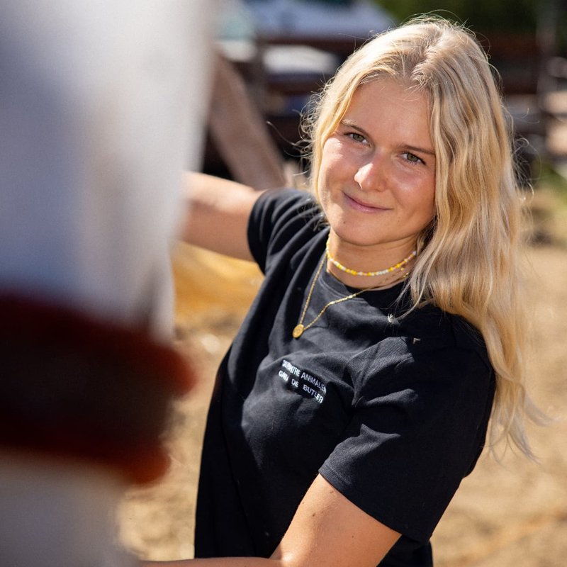Carla sourit près d'un cheval, t-shirt noir de l'ostéopathie animale