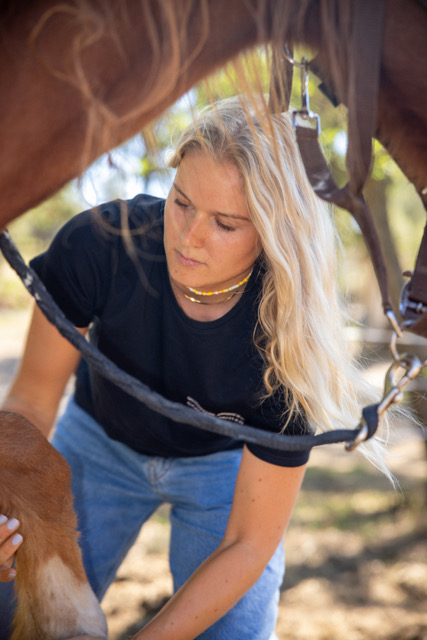 Carla se penche sous un cheval pendant une consultation